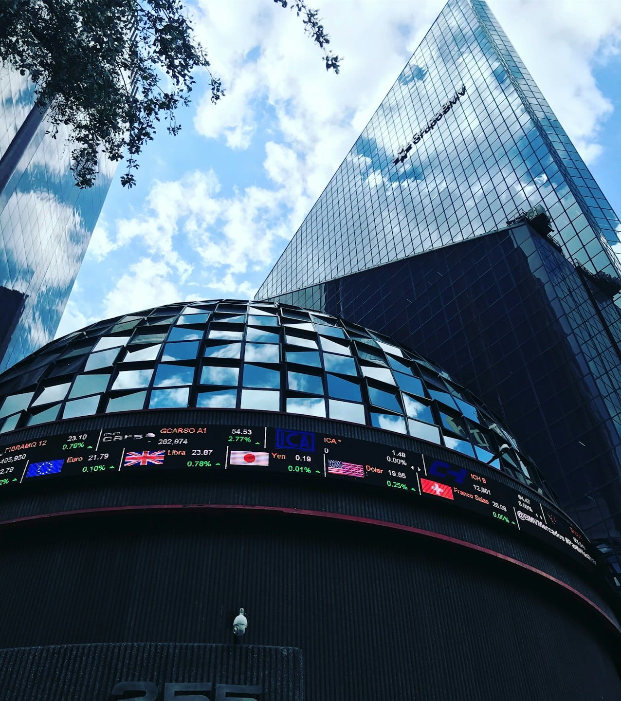 Edificio financiero moderno con pantalla digital bajo cielo azul.