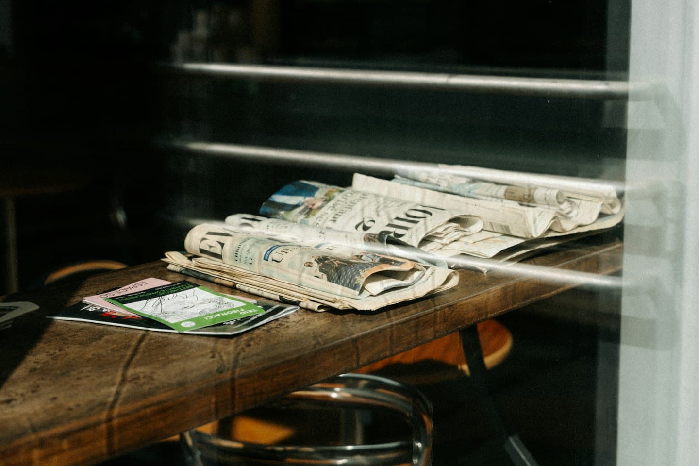 Periódicos doblados y un folleto verde sobre una mesa de madera.